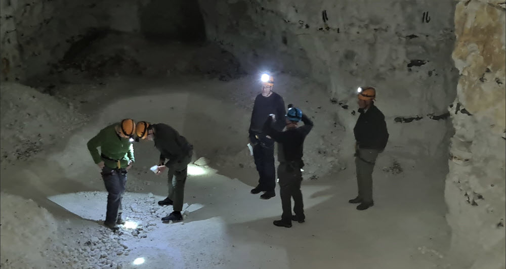 Five people with safety helmets and helmet lights standing on the floor of a chalk mine