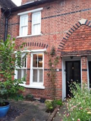 Victorian red brick terraced cottage on Park Street, Clewer. The two-storey property features white-painted sash windows, a decorative brick arch above the black front door, and a small front garden with shrubs and a blue planter. A tiled path leads to the entrance.