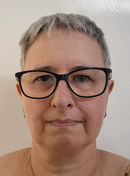 Vicki, a woman with short-cropped grey hair and black-rimmed glasses, looking directly at the camera in a headshot from June 2026.