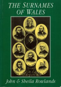 Book cover for "The Surnames of Wales" by John and Sheila Rowlands, featuring a green background and a central collage of nine vintage oval portraits of men labeled "Group M.C. Arfon".