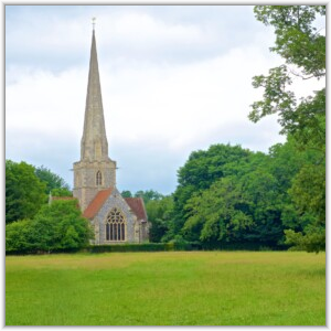 A historic stone church with a tall, slender spire and arched windows, nestled among lush green trees behind a grassy field.