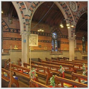Interior view of a church featuring wooden pews decorated with flowers, stone pillars supporting polychrome brick arches, and stained-glass windows.