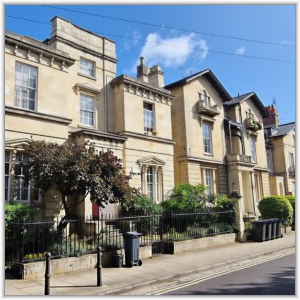A row of historic Victorian stone townhouses with wrought-iron railings and small front gardens along a sunny street.