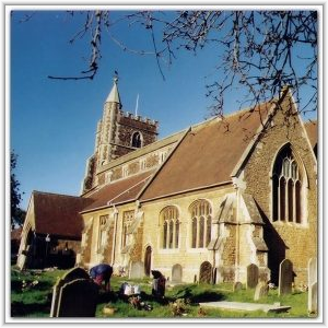 A historic stone parish church with a square tower and tiled roof, surrounded by headstones in a sunny churchyard.