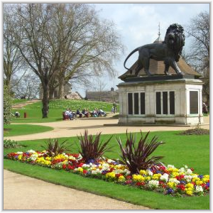 The bronze Maiwand Lion statue stands atop a stone memorial in Forbury Gardens, Reading, surrounded by colorful flower beds and manicured lawns.