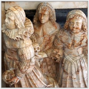 Carved stone effigies of three children in 17th-century period dress, each holding a skull on a historical church monument.