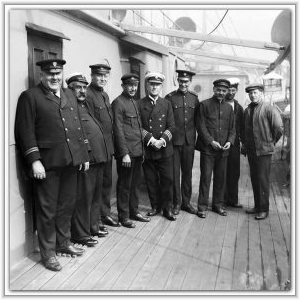 A group of nine uniformed ship officers and crew members pose together on the wooden deck of a vessel in a vintage black-and-white photograph.